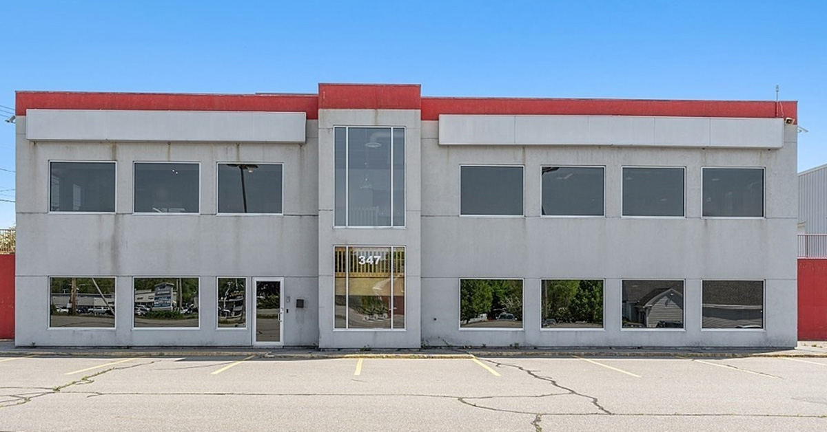 two story cement building with lots of windows and red trim at the roof line.